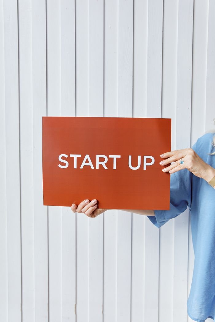 A person holding a sign reading 'START UP' against a white wooden backdrop.